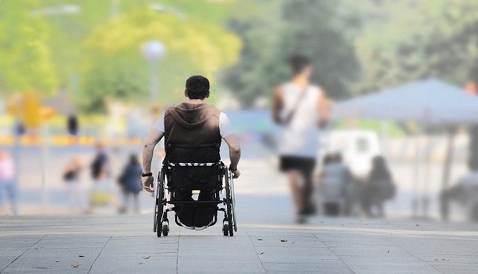 ASL affected young man on a wheel chair in the street among other people